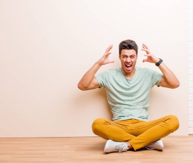 Genç Arap adam elleri havada bağırıyor. Öfkeli, sinirli, stresli ve üzgün bir şekilde yerde oturuyor.