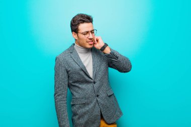 Genç Arap bir adam stresli, hayal kırıklığına uğramış ve yorgun hissediyor. Endişeli ve sorunlu bir bakışla mavi duvara yaslanıyor.