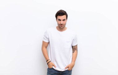 Genç yakışıklı, gururlu, kendine güvenen, havalı, küstah, küstah, gülümseyen, beyaz duvara karşı başarılı hisseden bir adam.