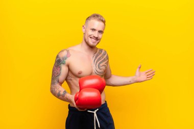 Genç sarışın güçlü adam mutlu ve neşeli hissediyor, gülümsüyor ve seni selamlıyor, dostça bir jestle seni boks eldivenleriyle içeri davet ediyor.