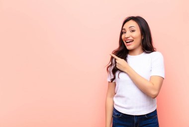 Genç Latin güzel kadın heyecanlı ve şaşırmış görünüyor. Yana ve yukarıya doğru düz duvara uzayı gösteriyor.