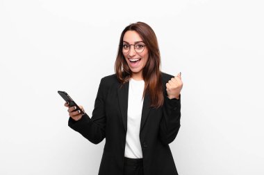 Genç iş kadını şok olmuş, heyecanlı ve mutlu hissediyor, gülüyor ve başarıyı kutluyor, vay canına! Ve elinde cep telefonu var.