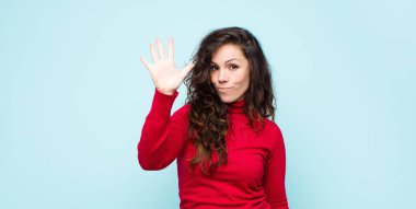 Genç, güzel bir kadın gülümsüyor ve arkadaş canlısı görünüyor. 5 ya da 5 numarayı gösteriyor. Elleri önde, mavi duvara doğru sayıyor.