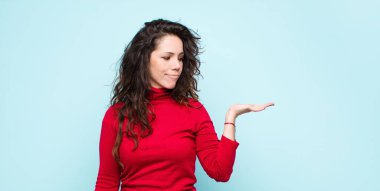 Genç, güzel bir kadın mutlu ve gülümsüyor. Mavi duvarın karşısında duran bir nesneye ya da konsepte bakıyor.