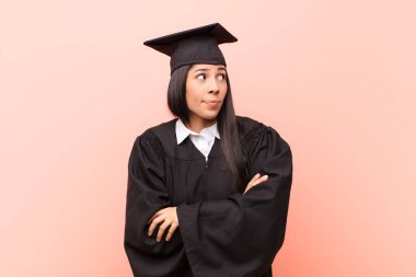 Genç Latin kız öğrenci omuz silkiyor, kafası karışık ve kararsız, kolları bağlı ve şaşkın görünüyor.