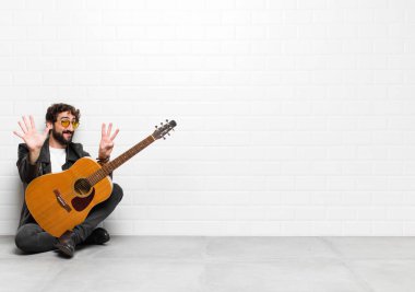 Genç müzisyen gülümsüyor ve arkadaş canlısı görünüyor, 8 ya da 8 numarayı gösteriyor, elleri önde, gitar, rock and roll konseptiyle geriye doğru sayıyor.