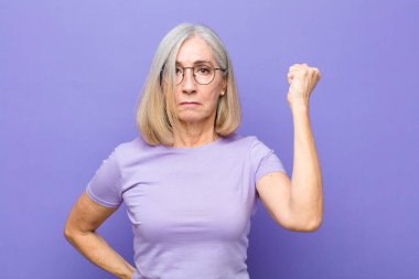 Yaşlı ya da orta yaşlı güzel bir kadın ciddi, güçlü ve asi hissediyor, yumruğunu kaldırıyor, protesto ediyor ya da devrim için savaşıyor.