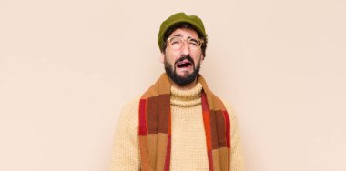 Genç havalı sakallı adam üzgün ve mızmız, mutsuz bir bakışla ağlıyor, olumsuz ve hayal kırıklığına uğramış bir tavırla.