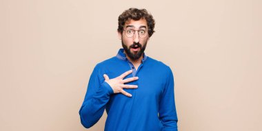 Genç yakışıklı adam şok olmuş, şaşırmış ve şaşırmış hissediyor, elleri göğsünde ve ağzı açık, kim diyor, ben mi? yassı duvara karşı