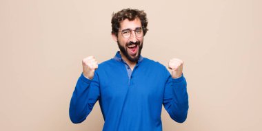 Genç yakışıklı adam mutlu, şaşırmış ve gururlu, bağırıyor ve başarıyı kutluyor. Düz duvara karşı kocaman bir gülümsemeyle.