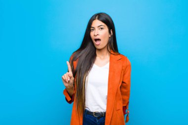 Genç, güzel Latin bir kadın bir fikri fark ettikten sonra mutlu ve heyecanlı bir dahi gibi hissediyor. Neşeli bir şekilde parmağını kaldırıyor. Evreka! yassı duvara karşı