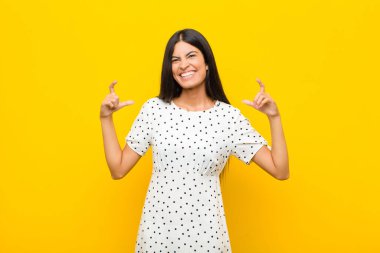 Genç, güzel, Latin bir kadın kendi gülüşünü çiziyor, iki eliyle, olumlu ve mutlu görünüyor, düz duvara karşı sağIık kavramı.