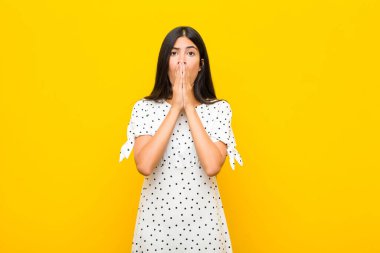 Genç, güzel, Latin bir kadın endişeli, üzgün ve korkmuş, elleriyle ağzını kapatmış, endişeli görünüyor ve düz duvara karşı her şeyi berbat ediyor.