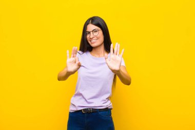 Genç ve güzel Latin kadın gülümsüyor ve arkadaş canlısı görünüyor, 8 ya da 8 numarayı gösteriyor, elleri önde, düz duvara doğru sayıyor