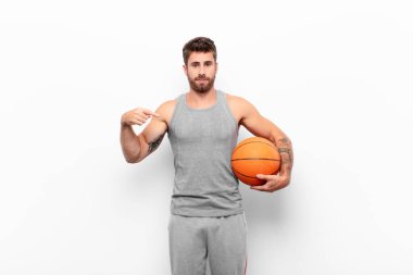 Genç ve yakışıklı bir adam gururlu, pozitif ve sıradan görünüyor. İki eli de basketbol topunu tutuyor..