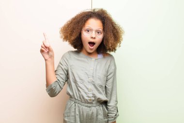 Afro-Amerikan küçük kızı bir fikri fark ettikten sonra mutlu ve heyecanlı bir dahi gibi hissediyor, neşeli bir şekilde parmağını kaldırıyor, eureka! yassı duvara karşı