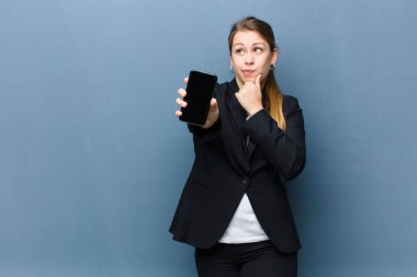 Genç sarışın kadın akıllı telefonu arka planda grunge duvarına karşı kullanıyor.