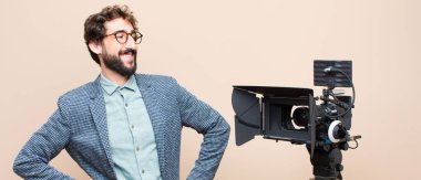 Televizyon sunucusu mutlu, neşeli ve kendinden emin görünüyor. Gururla gülümsüyor ve iki elini de kalçasında istiyor.