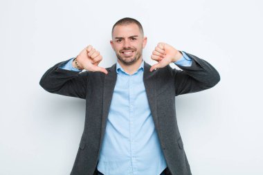 Genç işadamı üzgün, hayal kırıklığına uğramış ya da kızgın görünüyor, anlaşmazlık içinde parmaklarını gösteriyor, düz duvara karşı hayal kırıklığına uğramış hissediyor