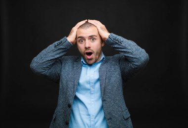 Genç işadamı heyecanlı ve şaşırmış görünüyor, ağzı açık, elleri başının üstünde, düz duvara karşı şanslı bir kazanan gibi hissediyor.