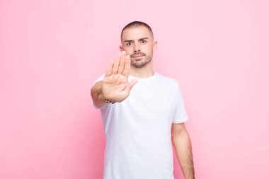 Genç yakışıklı adam ciddi, sert, hoşnutsuz ve kızgın görünüyor. Avuç içini açıp düz duvara karşı jest yapıyor.