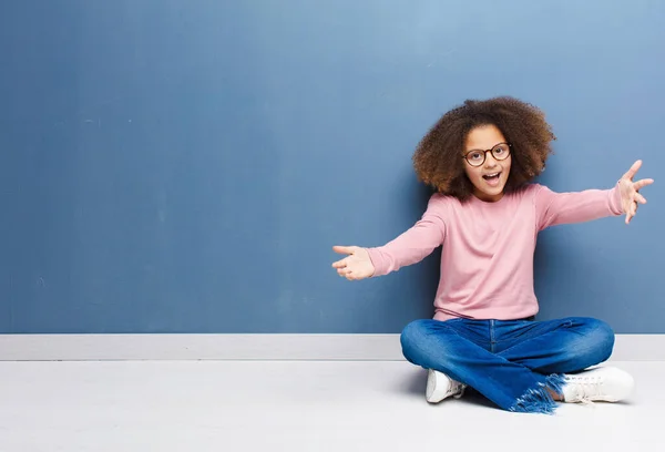 アフリカ系アメリカ人の少女が陽気に笑顔で温かくて友好的で愛情のこもった歓迎抱擁をし幸せを感じながら床に座り — ストック写真