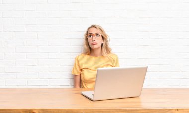 Genç, sarışın bir kadın üzgün ve mızmız görünüyor. Mutsuz bir bakışla ağlıyor. Olumsuz ve hayal kırıklığına uğramış bir tavırla dizüstü bilgisayar kullanıyor.