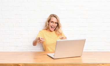 Genç sarışın kadın kendini mutlu, sakin, tatmin olmuş, rahat ve başarılı hissediyor, kameraya bakıyor, seni dizüstü bilgisayar kullanarak seçiyor.