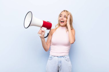 Genç sarışın kadın mutlu, heyecanlı ve şaşırmış hissediyor, iki eli yüzü megafonla yana bakıyor.