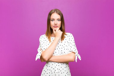 Kızıl saçlı güzel kadın ciddi, kafası karışmış, kararsız ve düşünceli görünüyor. Mor duvara karşı seçenekler veya tercihler arasında şüpheci.