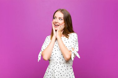 Kızıl saçlı, güzel bir kadın mutlu, heyecanlı ve şaşırmış, yüzünü mor duvara dayamış, yana bakıyor.