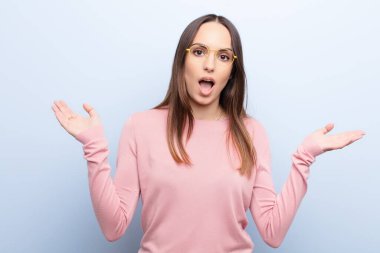 Genç, güzel bir kadın, mavi duvara karşı inanılmaz bir şey fark edince şaşırmış ve şaşırmış görünüyor.