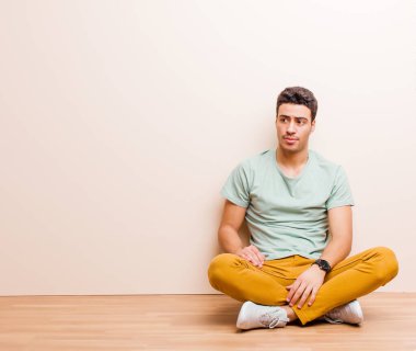 Genç Arap bir adam üzgün, üzgün ya da kızgın ve olumsuz bir tavır takınıyor, anlaşmazlık içinde yerde oturuyor.