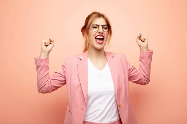 young pretty blonde woman feeling happy, surprised and proud, shouting and celebrating success with a big smile. business concept