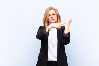 Orta yaşlı bir kadın sabırsız ve kızgın görünüyor, saati gösteriyor, dakiklik istiyor, zamanında gelmek istiyor.
