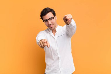 Genç yakışıklı adam mutlu ve kendinden emin, kamerayı iki eliyle gösteriyor ve gülüyor, seni seçiyor.