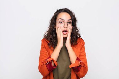 Genç ve güzel bir kadın şok olmuş ve korkmuş hissediyor. Ağzı açık ve elleri beyaz duvarda.