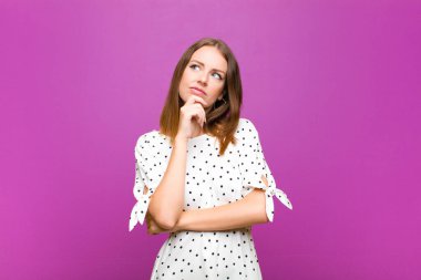 Kızıl saçlı güzel kadın, düşünüyor, kuşkulu ve şaşkın hissediyor, farklı seçeneklerle, mor duvara karşı hangi kararı vereceğini merak ediyor.