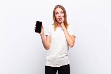 Kızıl saçlı güzel bir kadın şok olmuş ve korkmuş hissediyor, ağzı açık ve elleri akıllı bir telefon tutan ellerle dehşete düşmüş görünüyor.