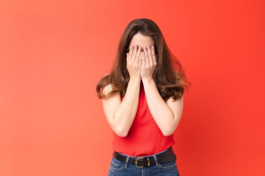 Genç, güzel bir kadın üzgün, hayal kırıklığına uğramış, gergin ve depresif, yüzünü iki eliyle kapatıyor, kırmızı duvara karşı ağlıyor.