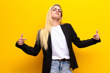 Genç, güzel sarışın kadın gururlu, kibirli, mutlu, şaşırmış ve tatmin olmuş görünüyor, kendini gösteriyor, sarı duvara karşı kazanan gibi hissediyor.