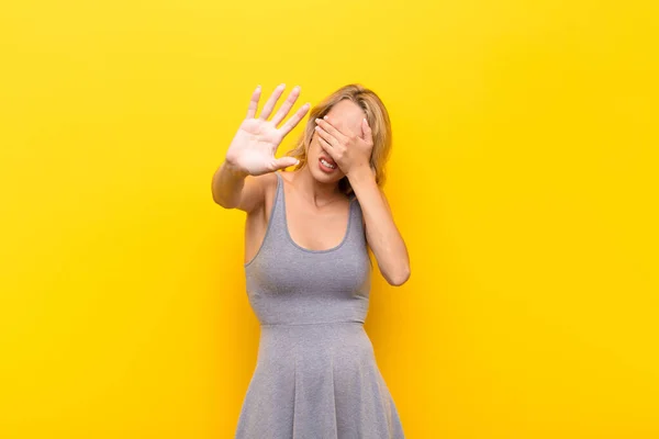 年轻的金发女人用手捂住脸 把另一只手放在前面挡住相机 拒绝拍照或照片贴在橙色墙上 — 图库照片