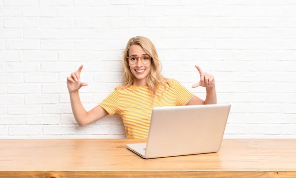 young blonde woman framing or outlining own smile with both hands, looking positive and happy, wellness concept using a laptop