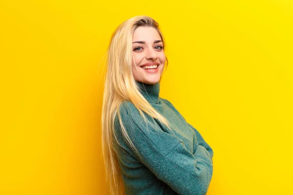 腕を組んでカメラに微笑む若い金髪の若い女性と幸せそうで自信満々の表情黄色の壁に対する横の見方 — ストック写真