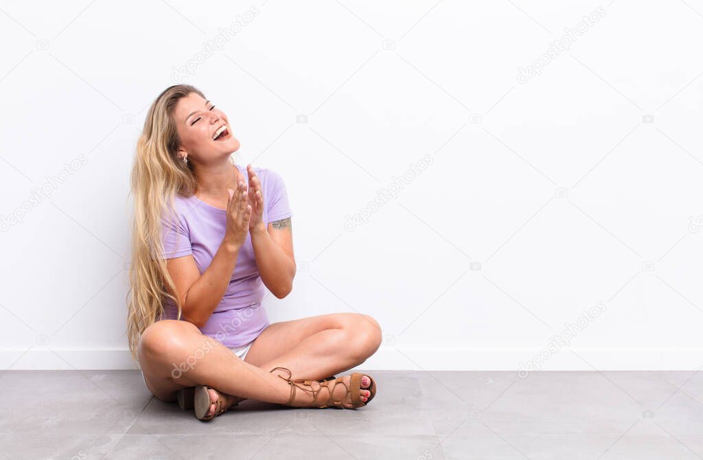 young pretty latin woman feeling happy and successful, smiling and clapping hands, saying congratulations with an applause sitting on the floor