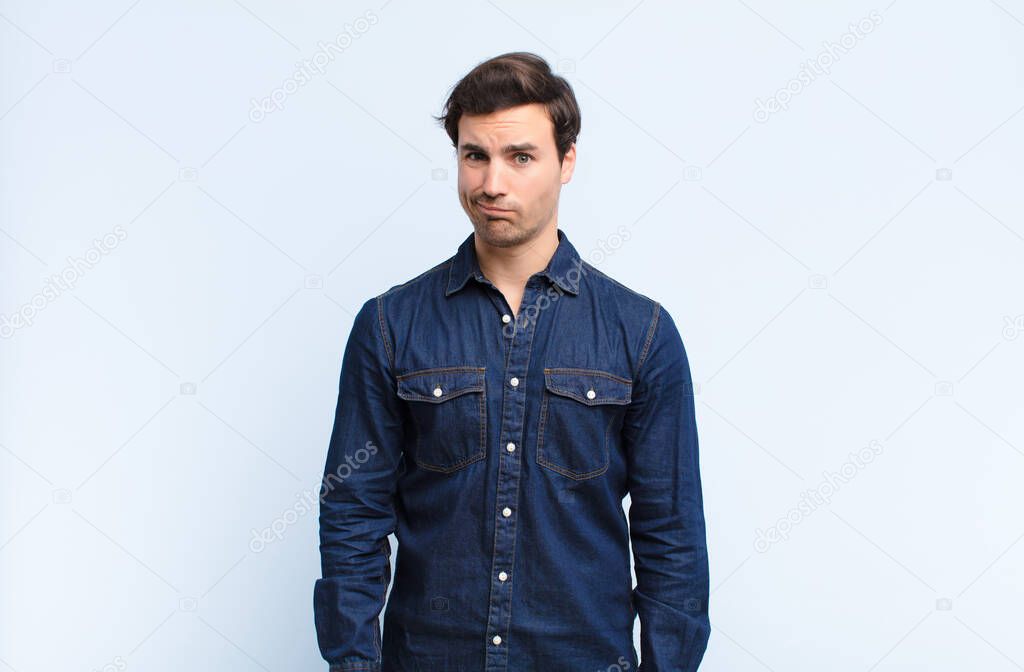 young handsome man feeling confused and doubtful, wondering or trying to choose or make a decision against blue wall