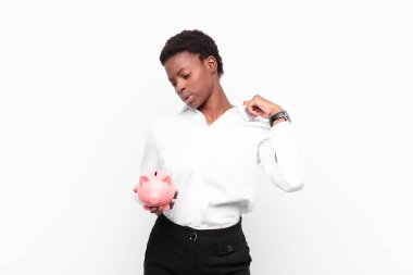 Genç siyahi kadın stresli, endişeli, yorgun ve hayal kırıklığına uğramış, gömleğini çekiştirmiş, domuz kumbarası tutmakta zorlanıyor gibi görünüyor.