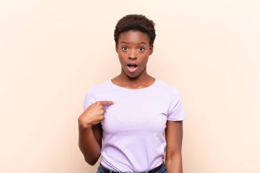 Genç, güzel, siyah bir kadın ağzı açık ve şaşkın bir şekilde kendini işaret ediyor.