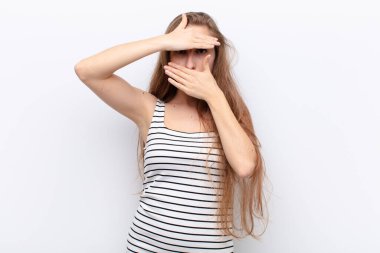 Genç sarışın kadın kameraya hayır diyen iki eliyle yüzünü kapatıyor! Resimleri reddetmek ya da beyaz duvara karşı resimleri yasaklamak