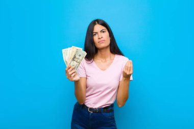 Genç ve güzel Latin bir kadın kapiş ya da para hareketi yapıyor, sana borçlarını ödemeni söylüyor! yassı duvara karşı